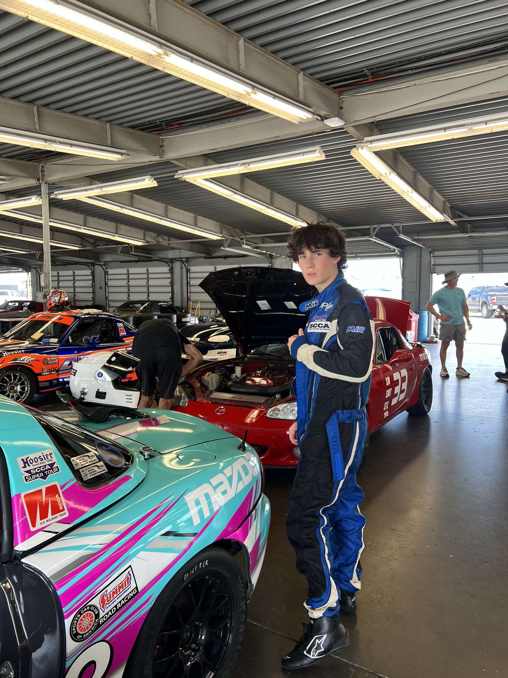 Hayden standing in the garage between two OPM Racing Spec Miatas